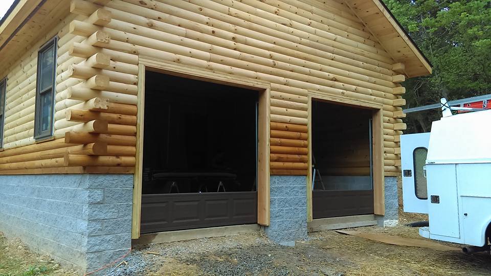 Log garage with two brown garage doors and a white service van.