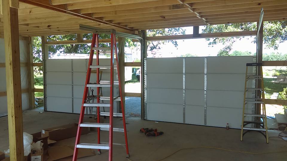 Garage under construction with red ladder, white garage doors, and wooden framework.