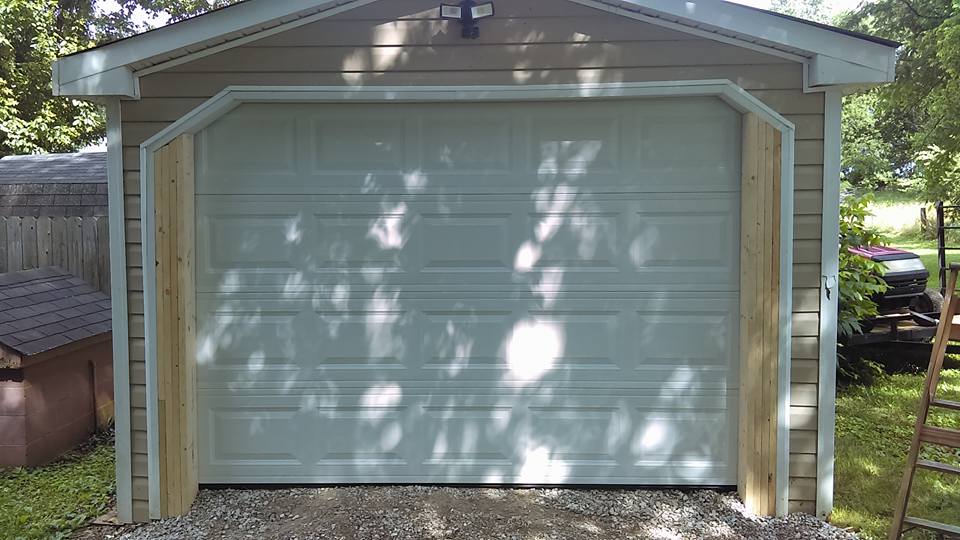 Garage with white door, light-colored wooden trim, and gray gravel driveway. Trees cast shadows.
