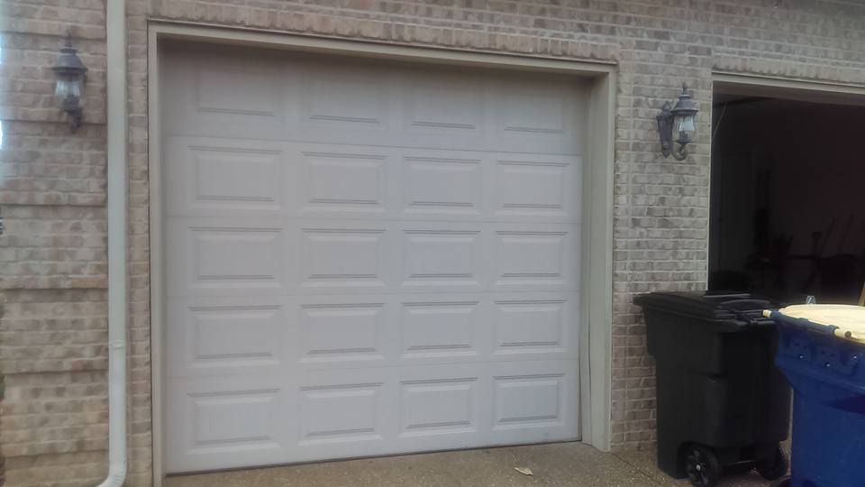 White garage door on brick building with trash cans.
