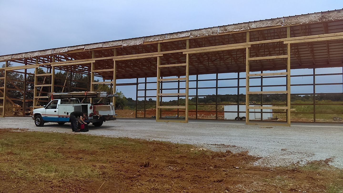 Construction of a large wooden frame building. A truck sits near the building on a gravel lot.