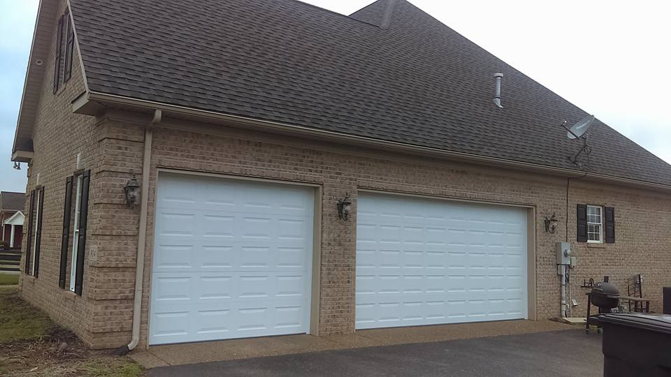 Brick house with two white garage doors and brown roof.