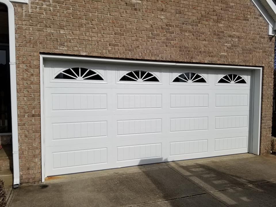 White garage door with four top windows and brick wall.