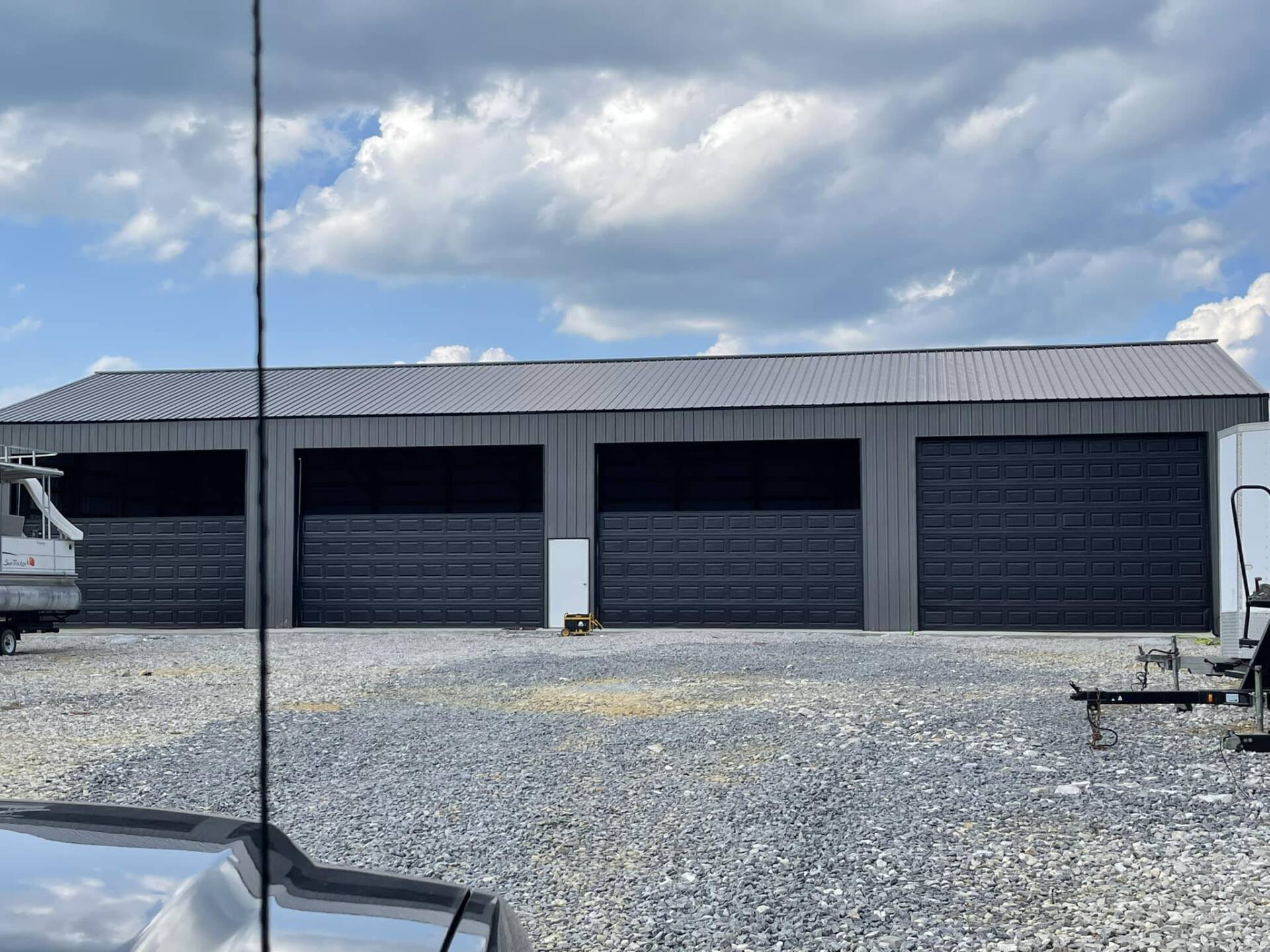 Gray metal garage with four bays, on a gravel lot, under a cloudy sky.
