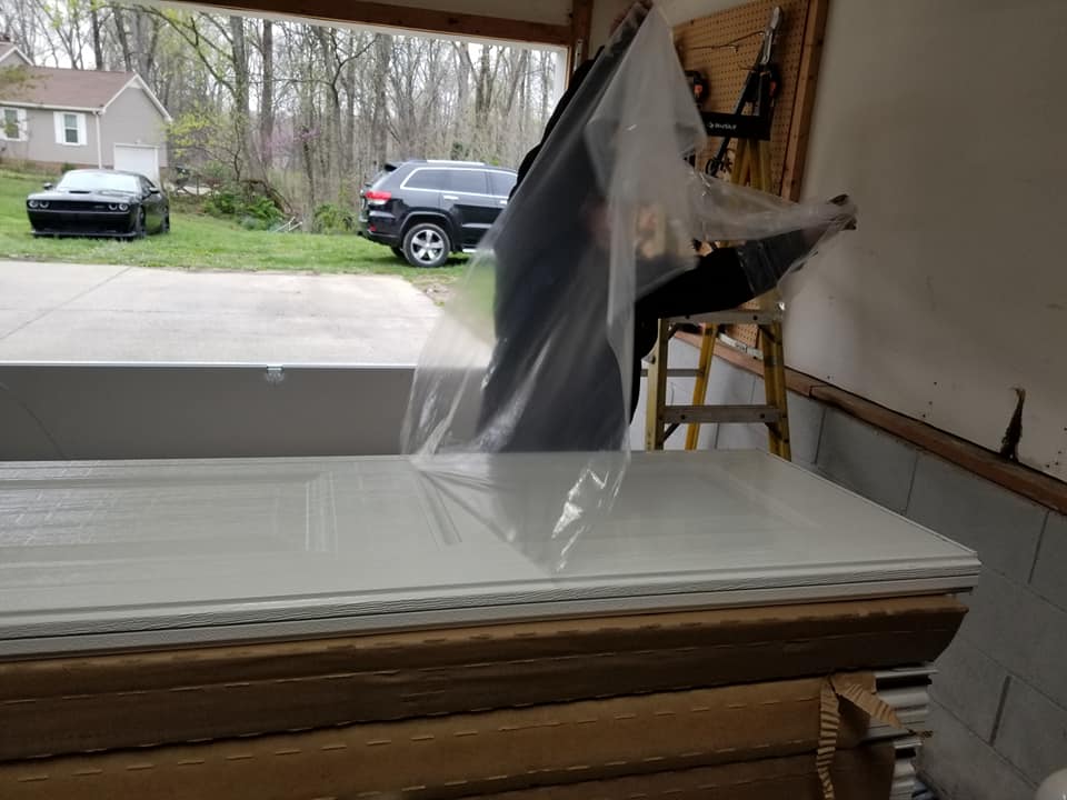 Person removing plastic wrap from a white door inside a garage. Cars are visible outside.