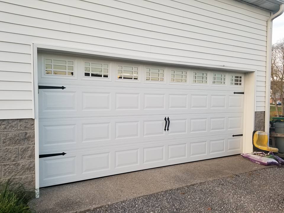 White garage door with windows, black hardware, set in front of a white building with concrete block foundation.