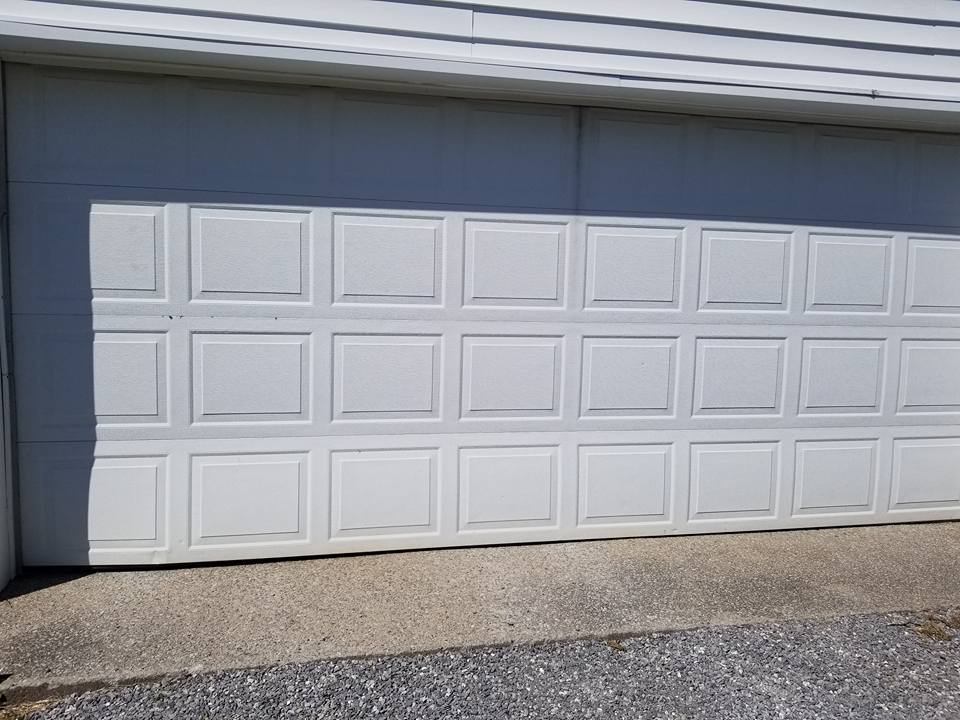 White garage door with recessed square panels, partially open, against a light-colored building.