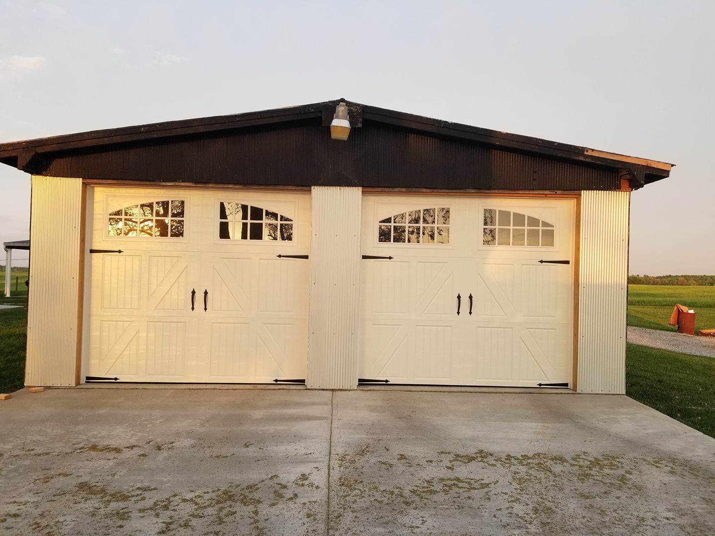 Two-car garage with white doors, dark brown roof, and corrugated metal siding on a concrete slab.