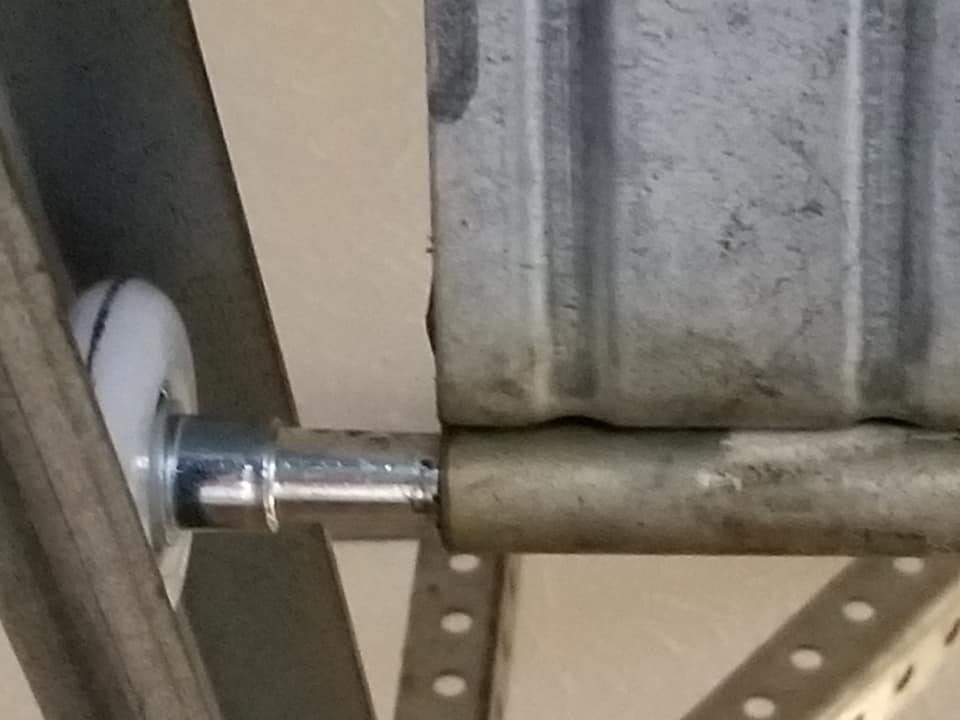 White roller on a metal shaft, between a metal frame and garage door panel.