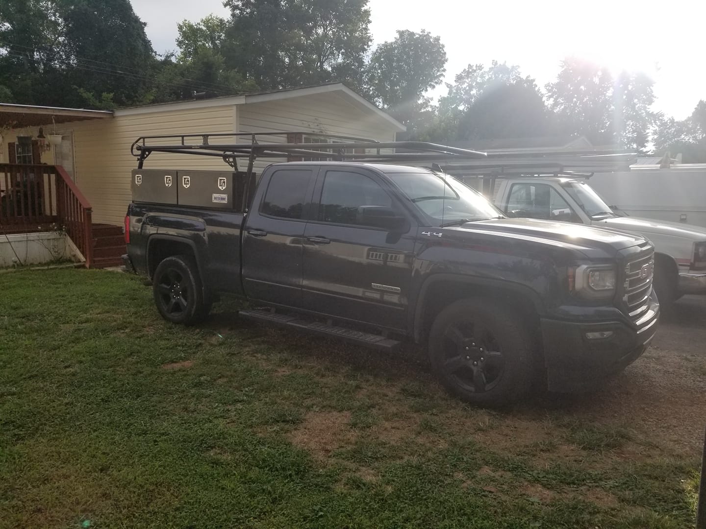 Dark pickup truck with black wheels, equipped with a ladder rack and storage boxes.