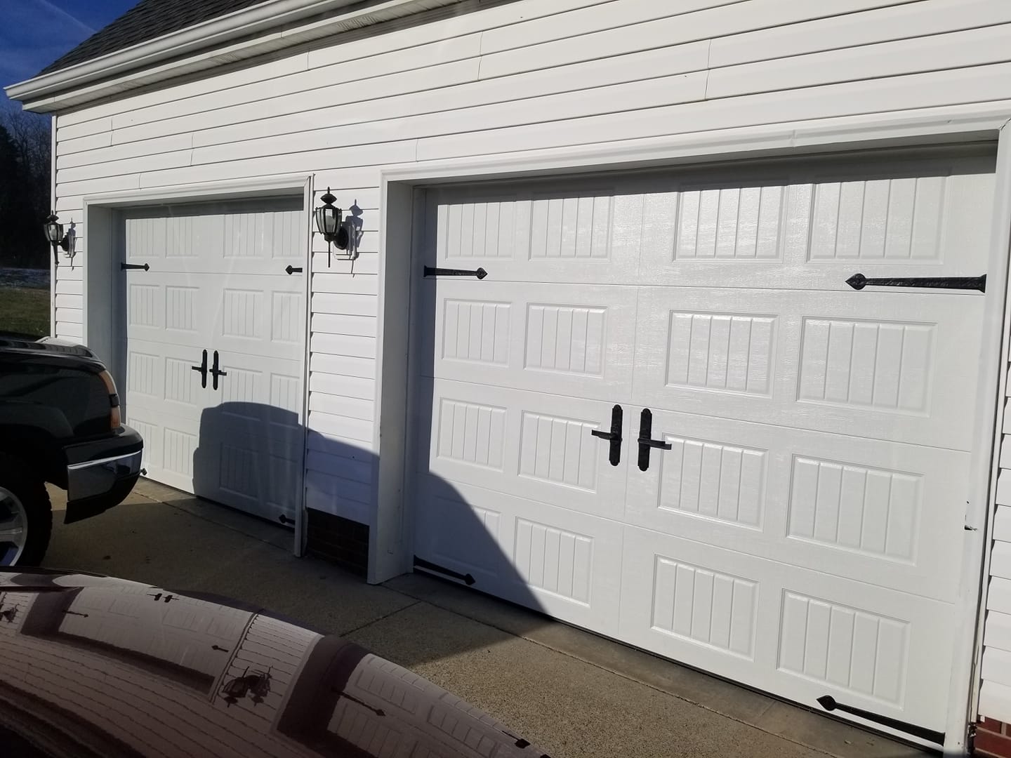White two-car garage with black decorative hardware. A black vehicle is partially visible.