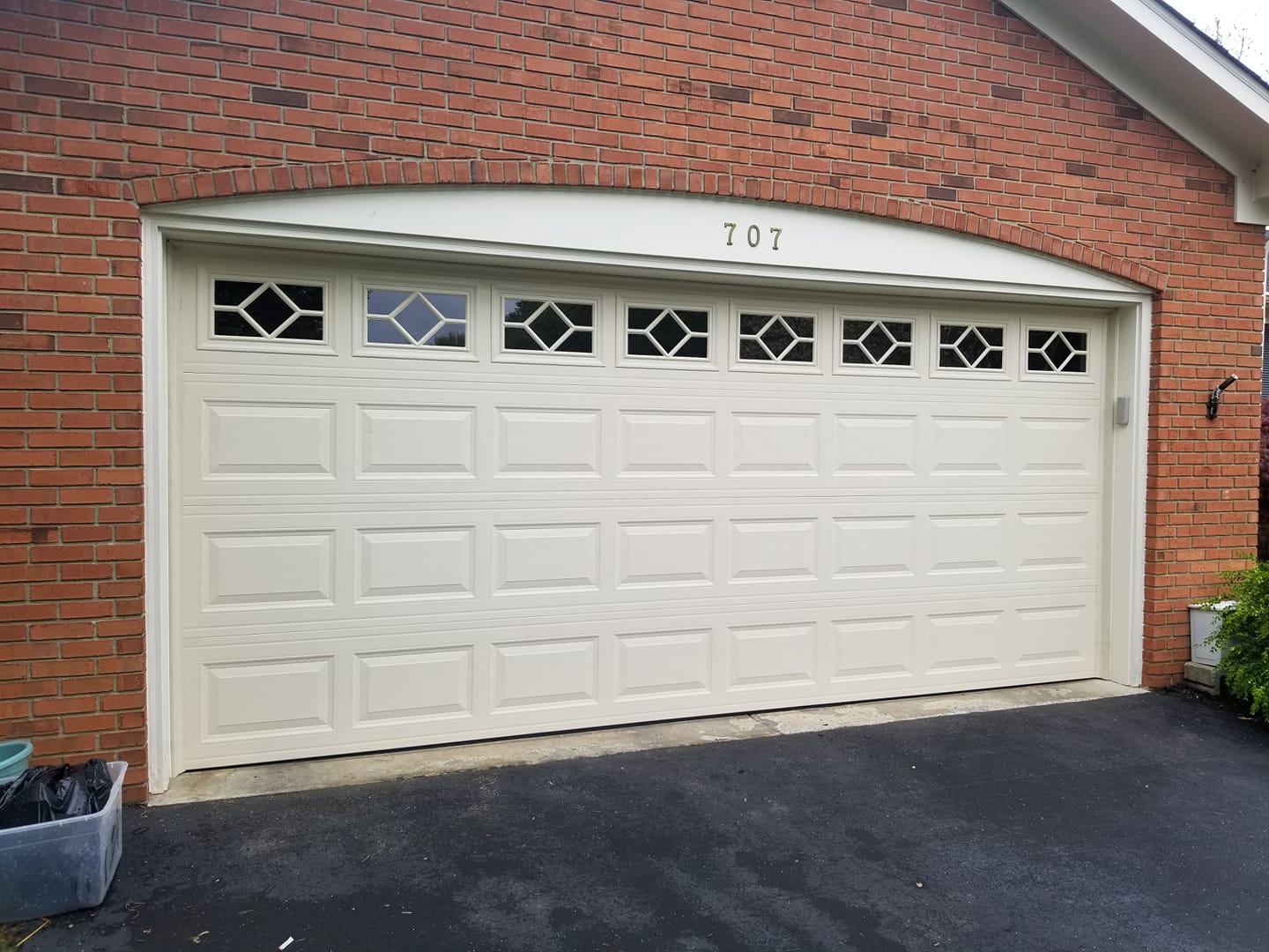 Cream-colored garage door with diamond-shaped windows, set in a brick building. House number 107 above the door.