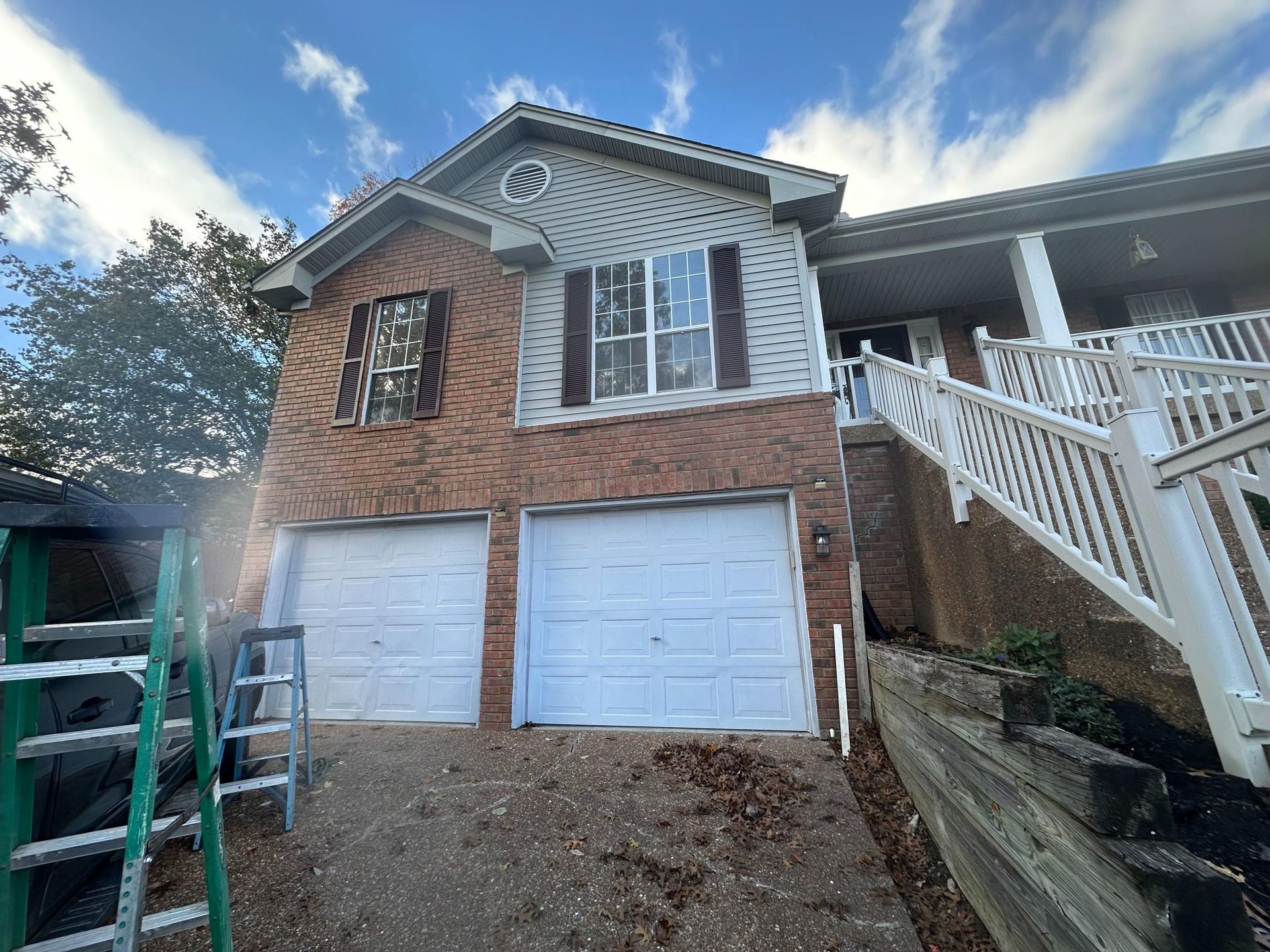 Two-story brick house with white garage doors and siding. A staircase leads to a covered porch.