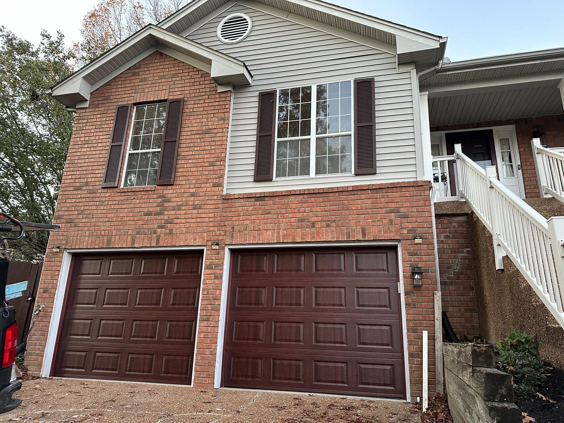 Two-story brick house with brown garage doors and shutters. Staircase leads to the front door.