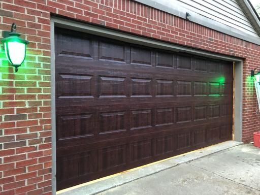 Dark brown garage door, brick building with a green light on the wall.