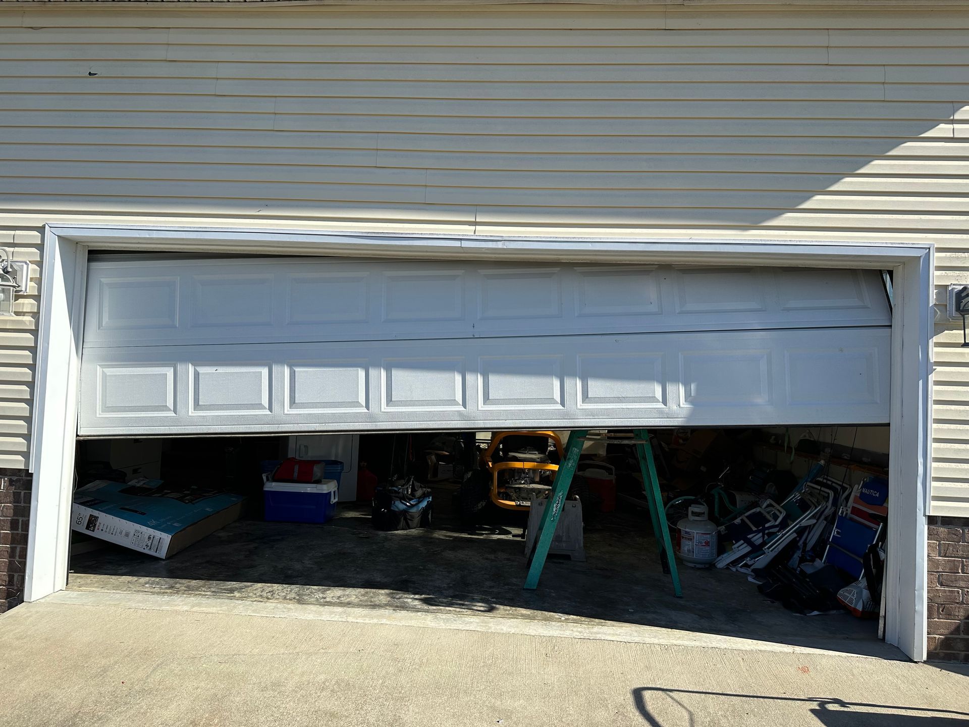 White garage door partially open, revealing cluttered interior, tools, and a green ladder.