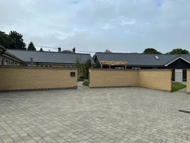 A brick driveway leading to a house with a fence around it.