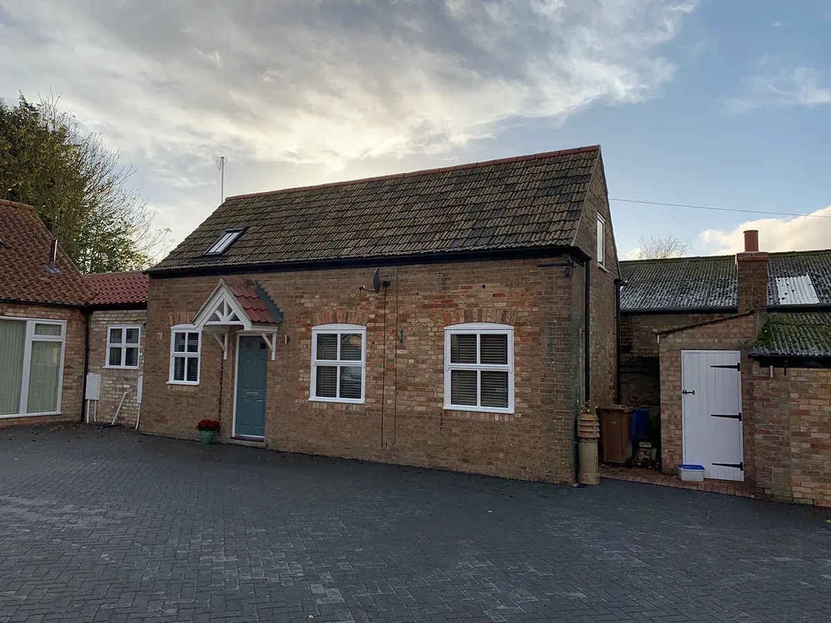 A small brick house with a roof and a driveway in front of it.