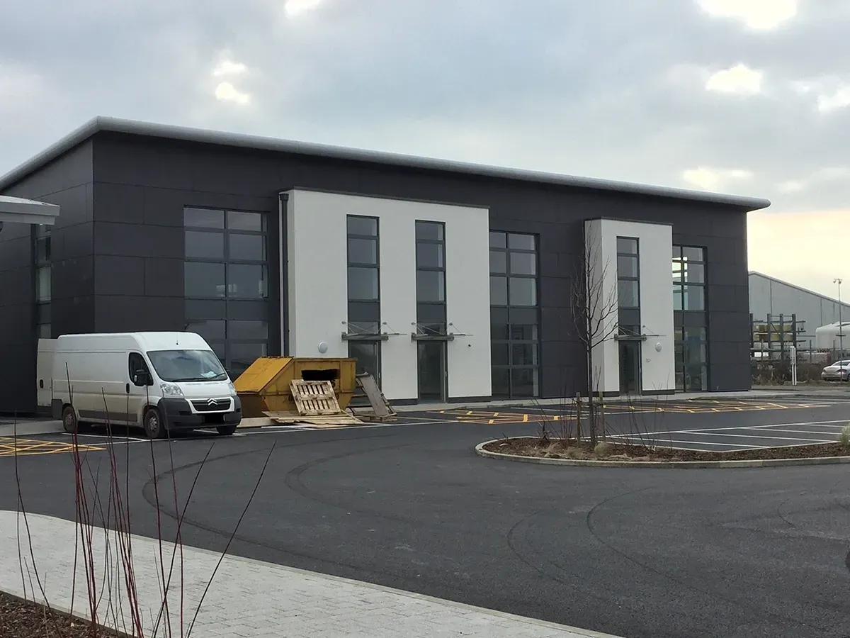 A white van is parked in front of a large building.