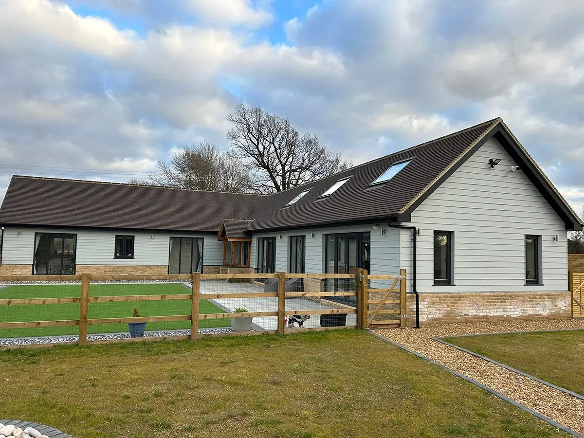A white house with a brown roof and a wooden fence in front of it.