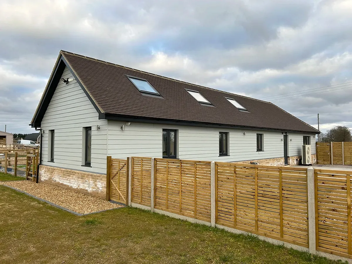 A white house with a brown roof and a wooden fence in front of it.