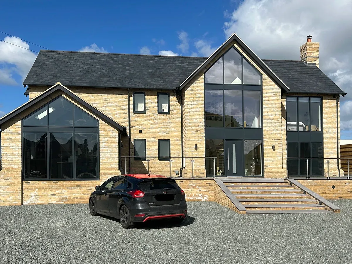 A car is parked in front of a large house with a lot of windows.