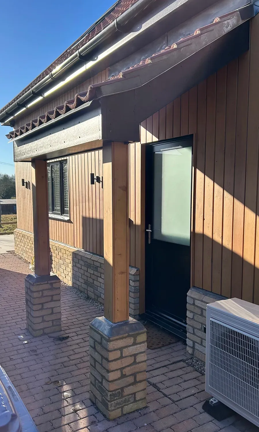 A wooden house with a black door and a white air conditioner on the side of it.