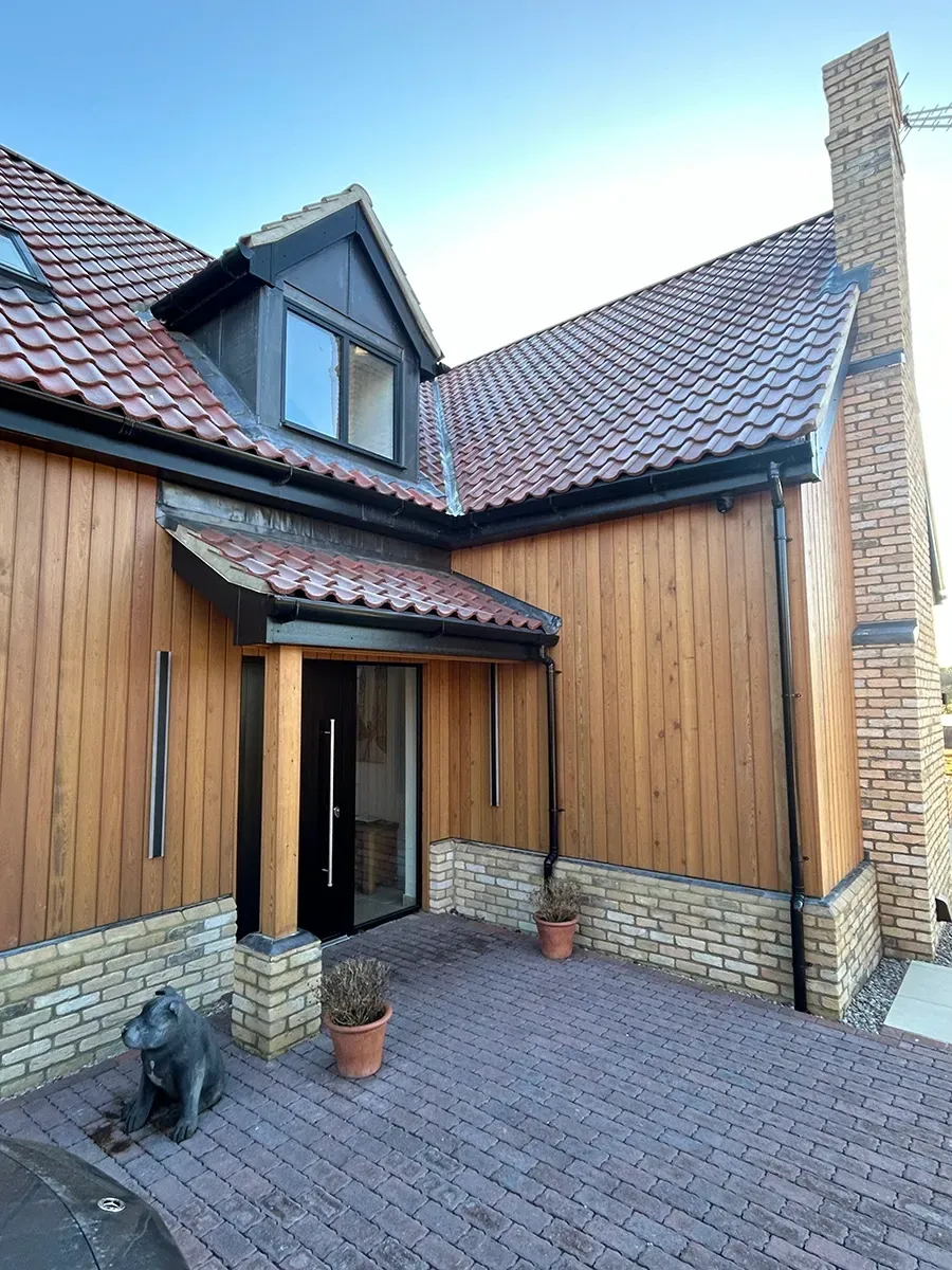 A large wooden house with a red tiled roof and a brick driveway.