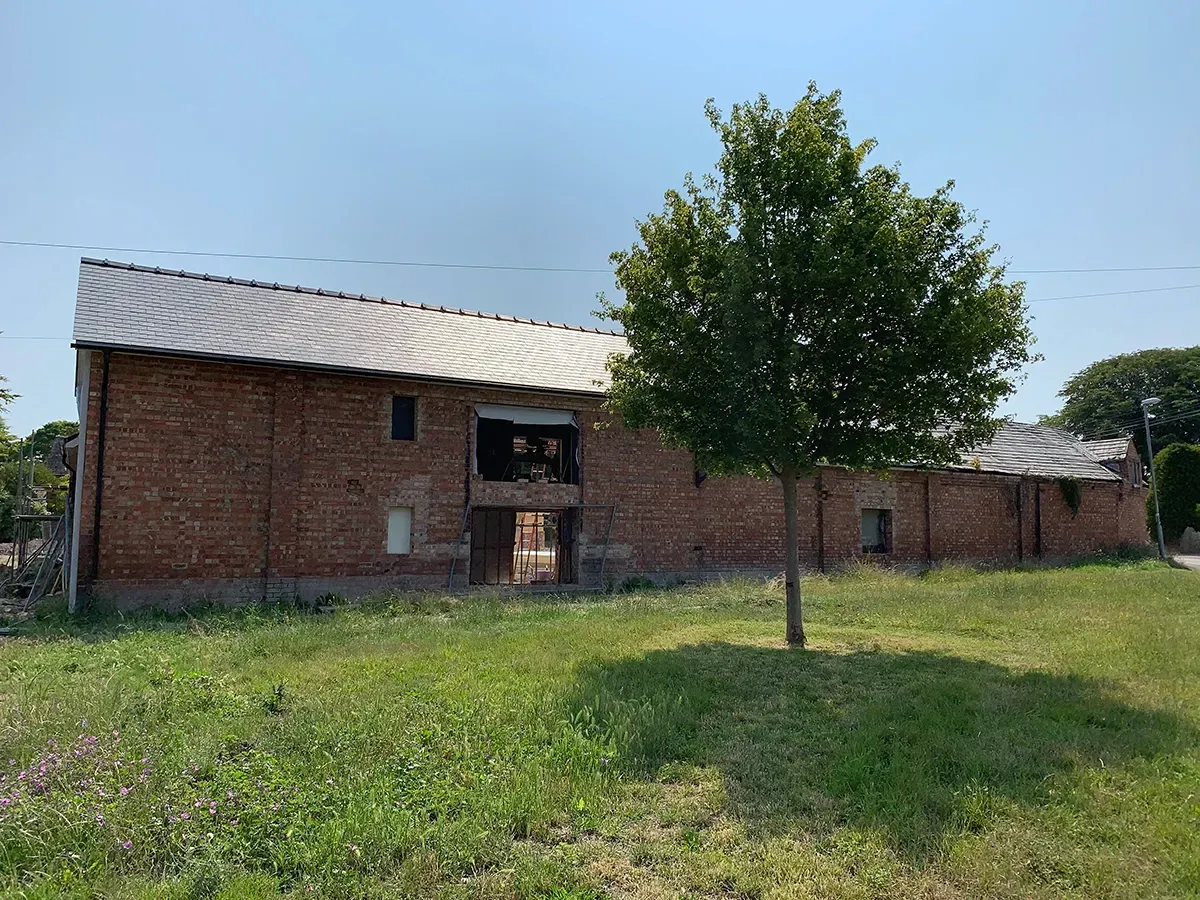 A large brick building is sitting in the middle of a grassy field next to a tree.