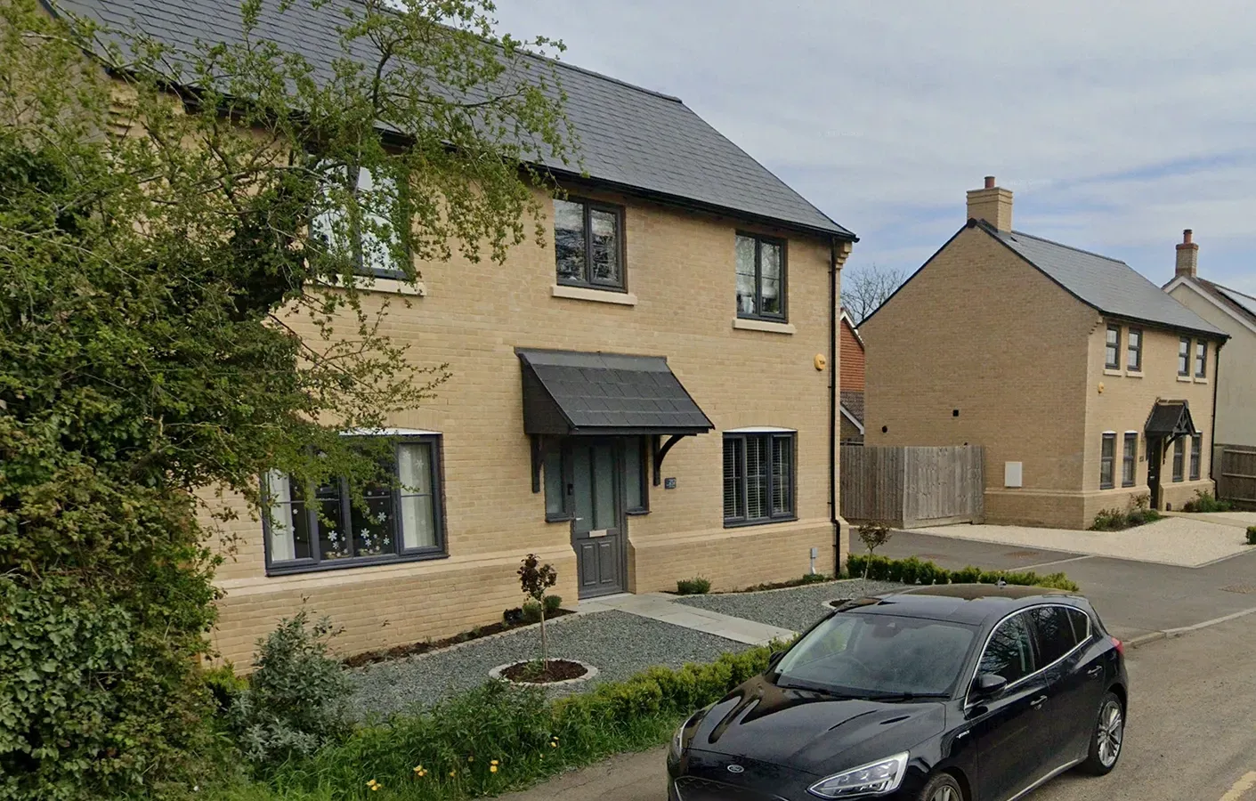 A black car is parked in front of a brick house.