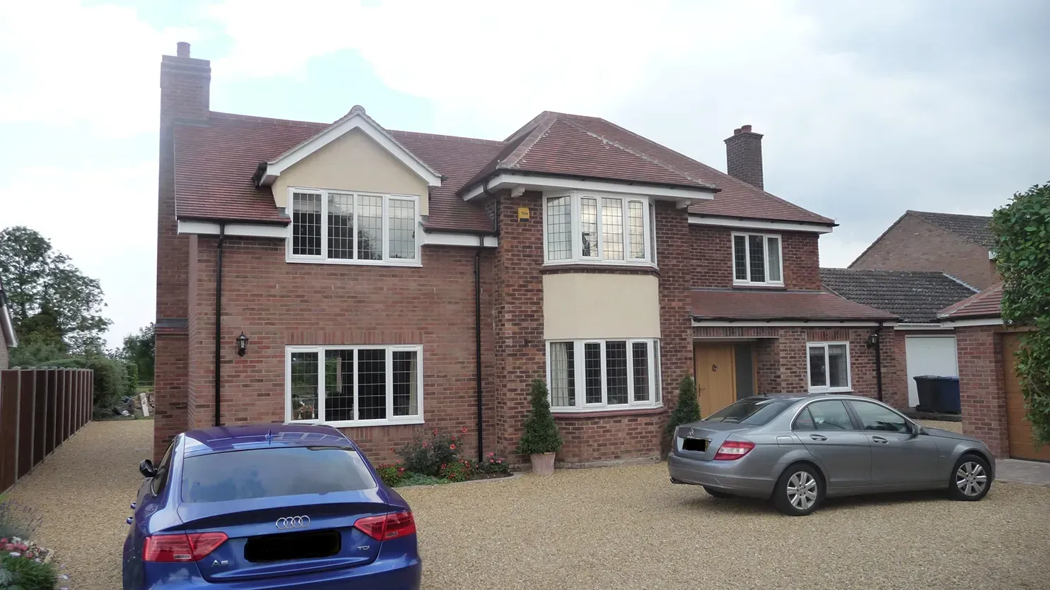 A blue car is parked in front of a large brick house