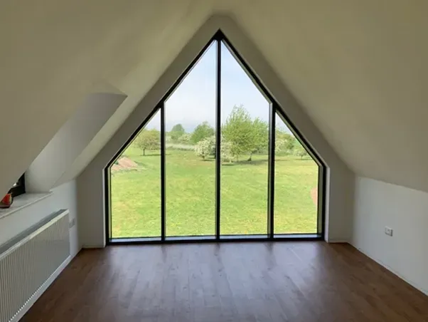 An empty room with a large triangle shaped window overlooking a field.