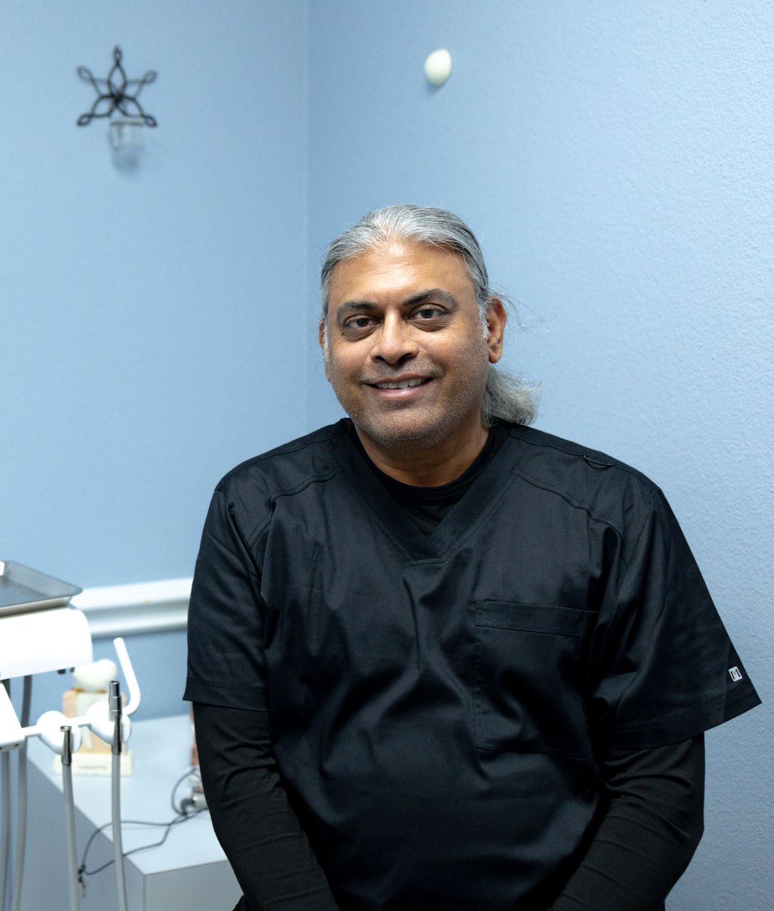 Smiling person in black scrubs in a blue-walled office.