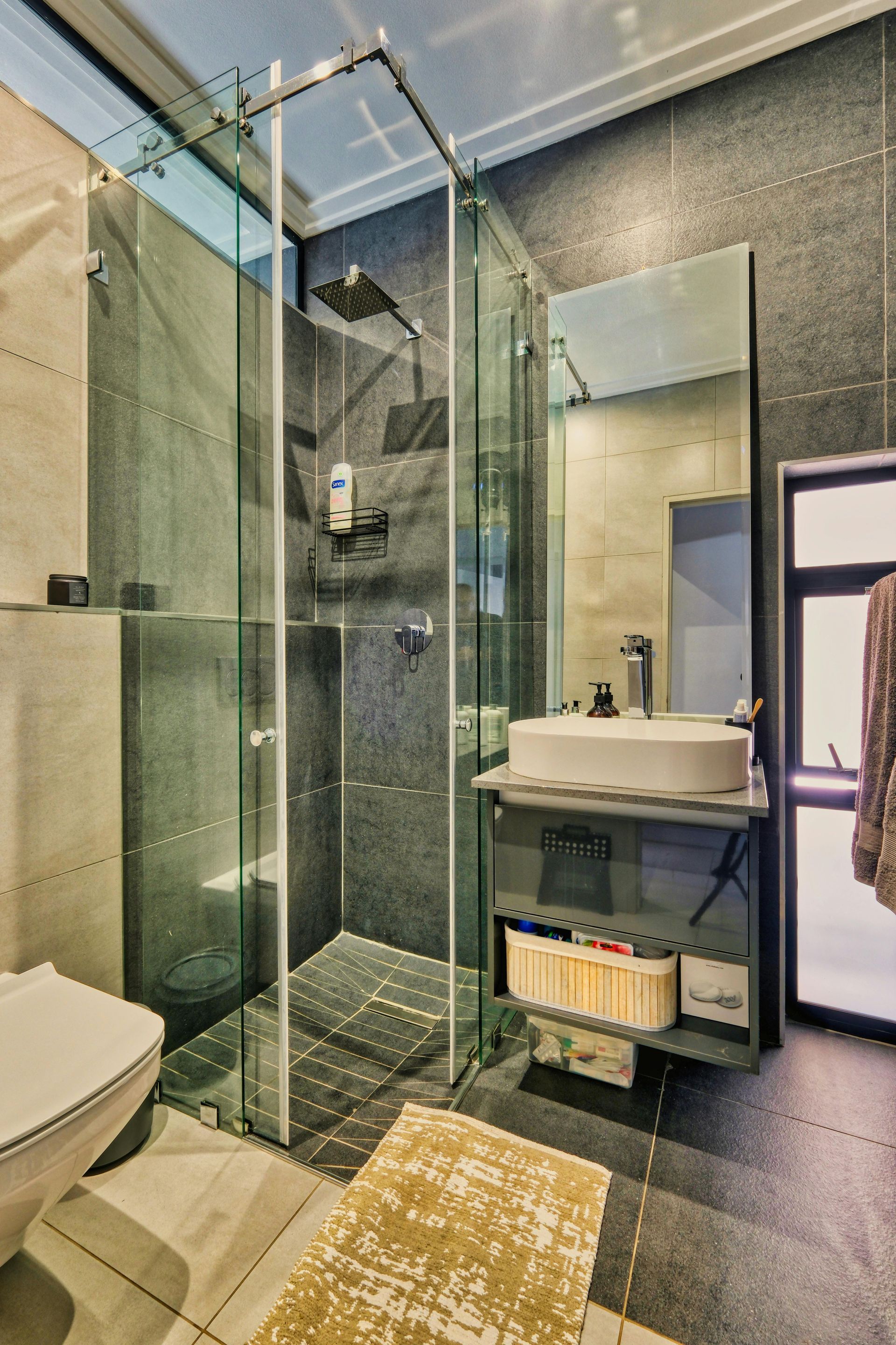 tall bathroom with enclosed shower with black floor and wall tiles
