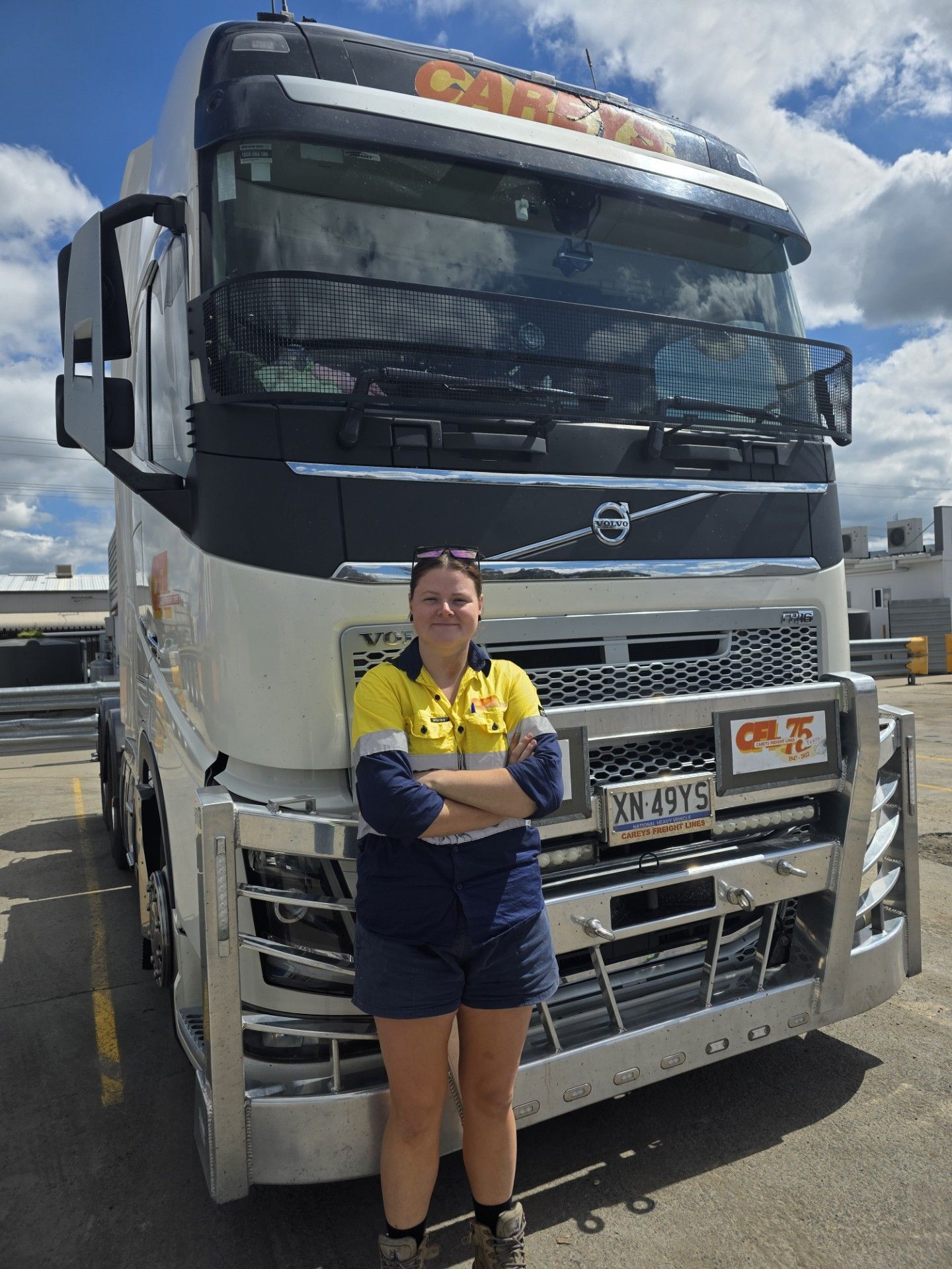 Woman driving a truck, wearing a safety vest, looking ahead, sunny outdoors.