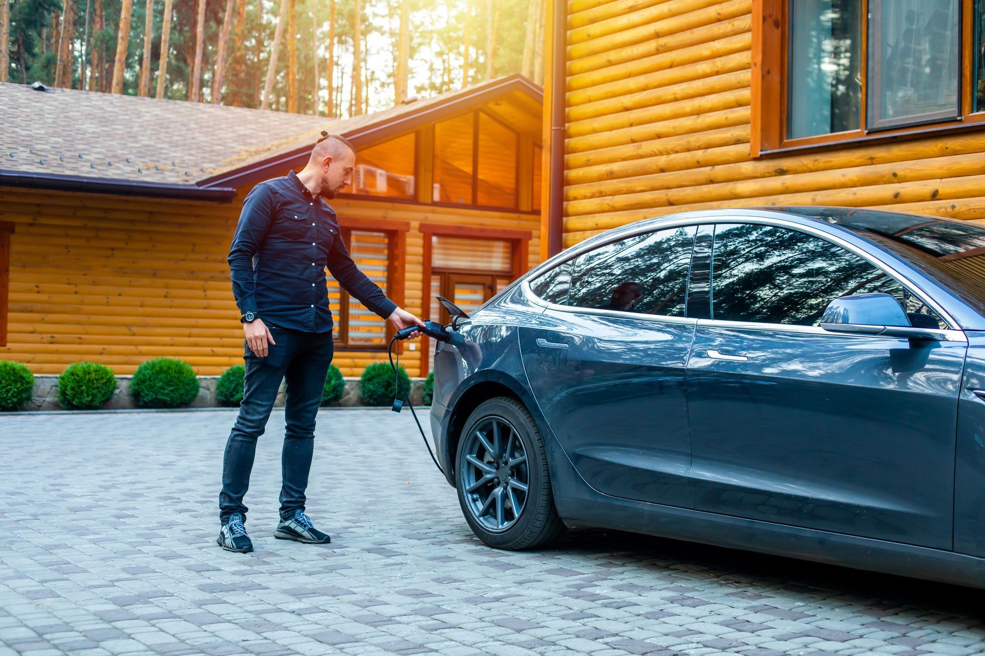 A man connecting a charging cable to a car from an electric car charging station by a townhouse.