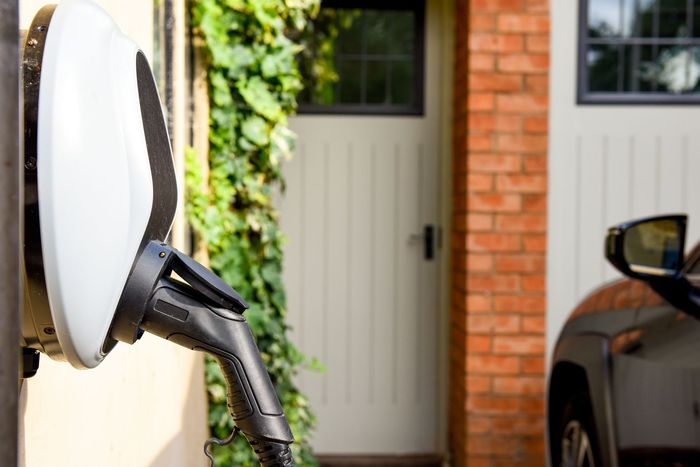 An electric car is plugged into an EV charge station outside the home with a power cable. An electric car is plugged into an EV charge station outside the home with a power cable.