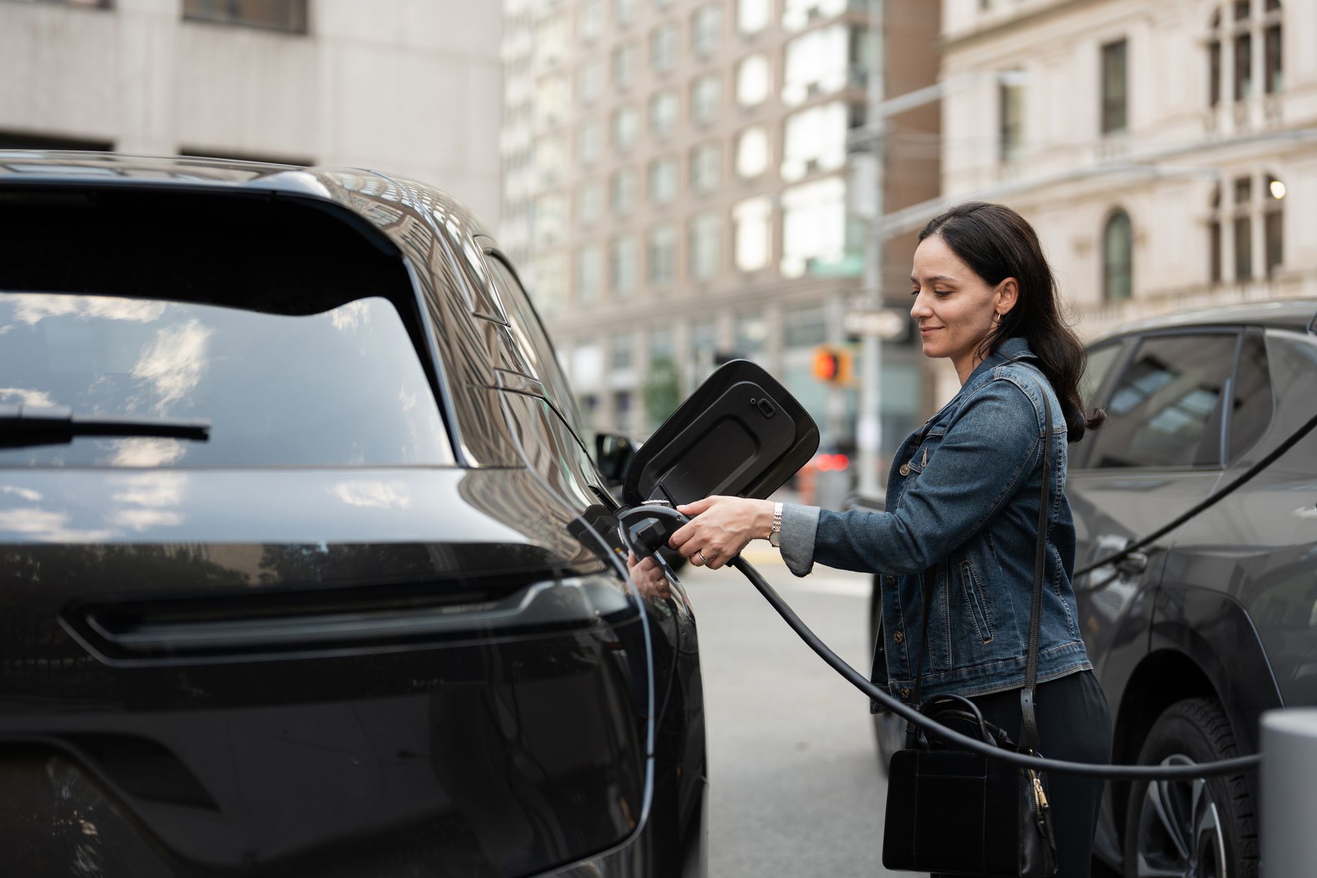 Woman plugging in an electric vehicle in an urban setting.