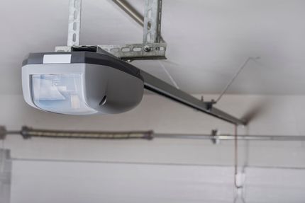 Garage door opener mounted on the ceiling with a metal track and spring in a garage.