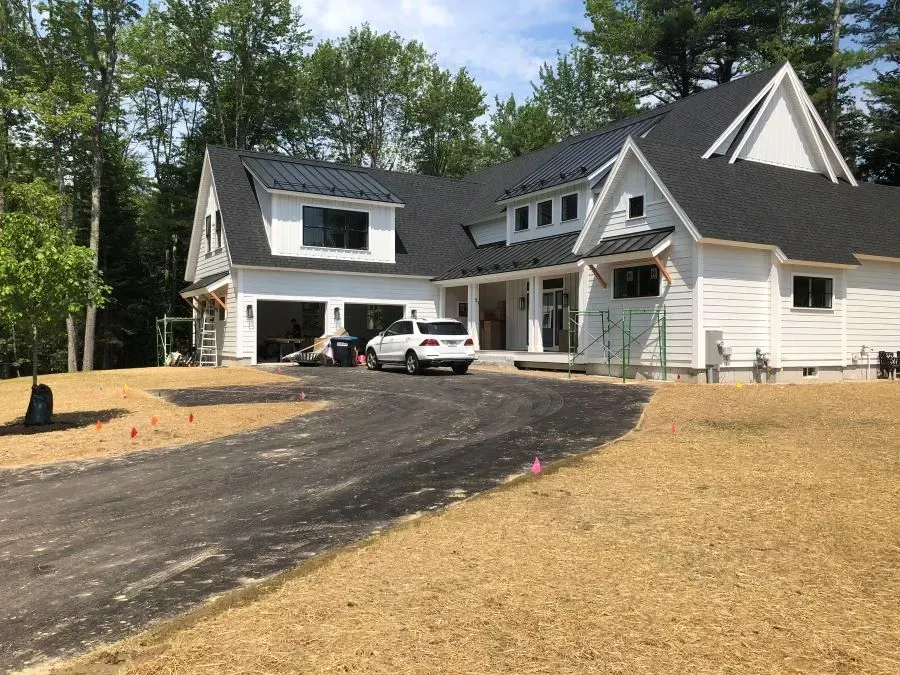 A white car is parked in front of a large white house.