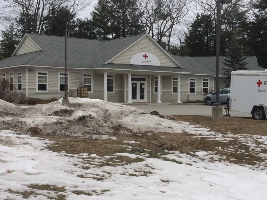 A white van with a red cross on it is parked in front of a building