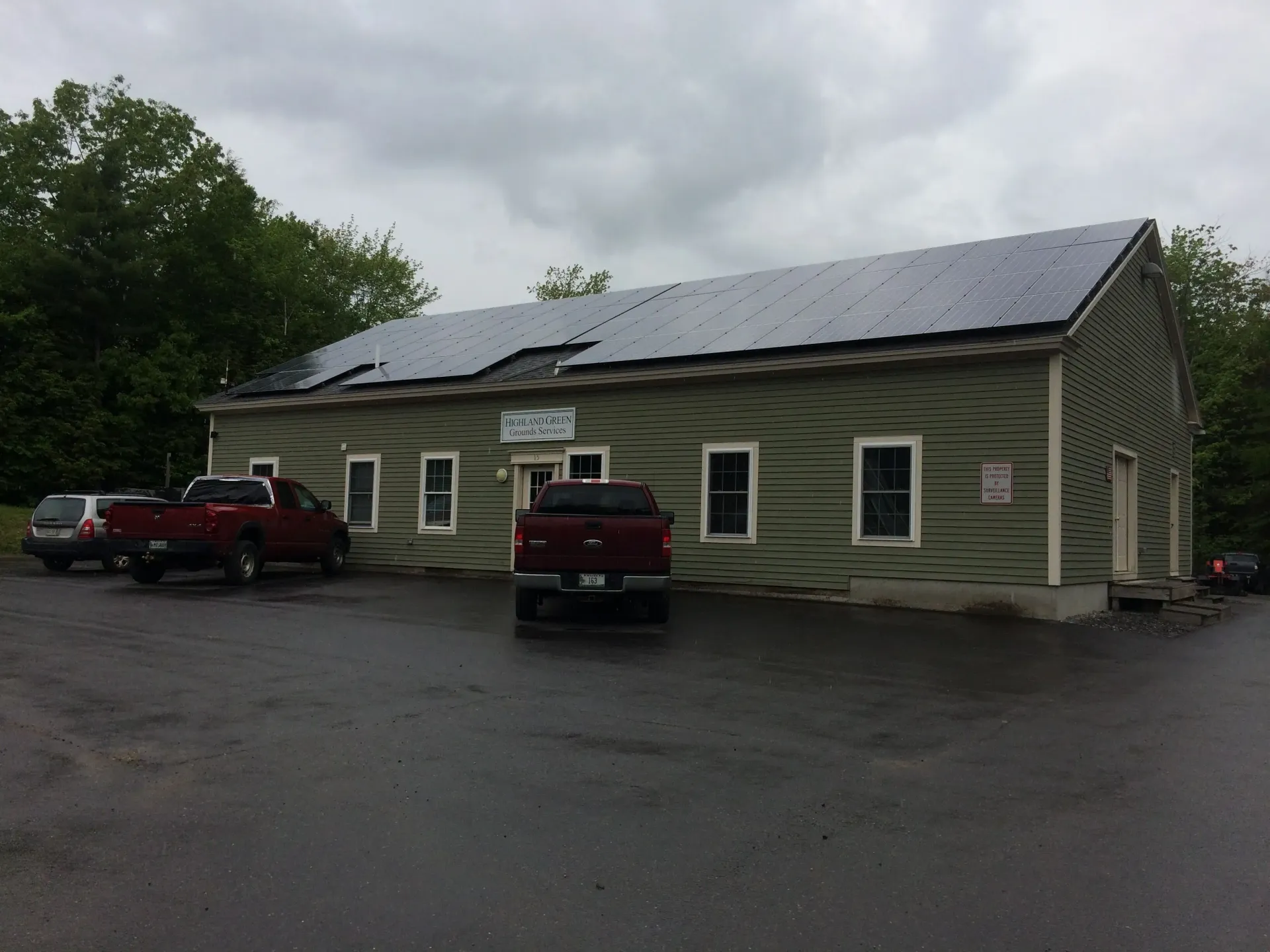 Two red trucks are parked in front of a building with solar panels on the roof.