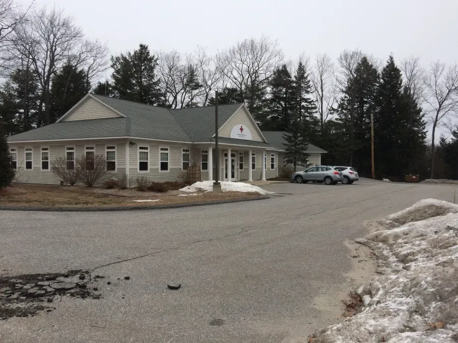A white house with a gray roof is surrounded by snow and trees
