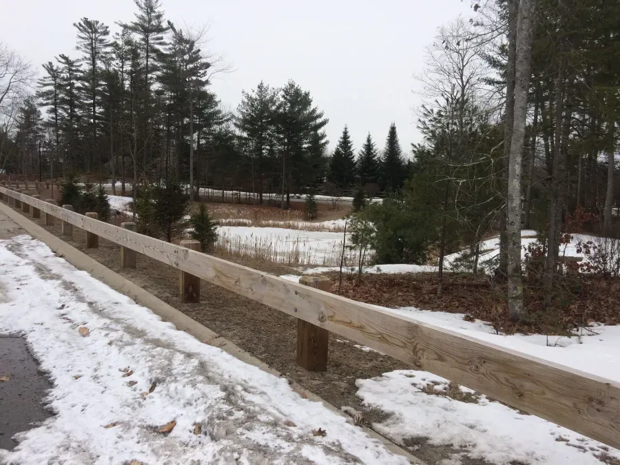 A snowy road with a wooden fence and trees in the background