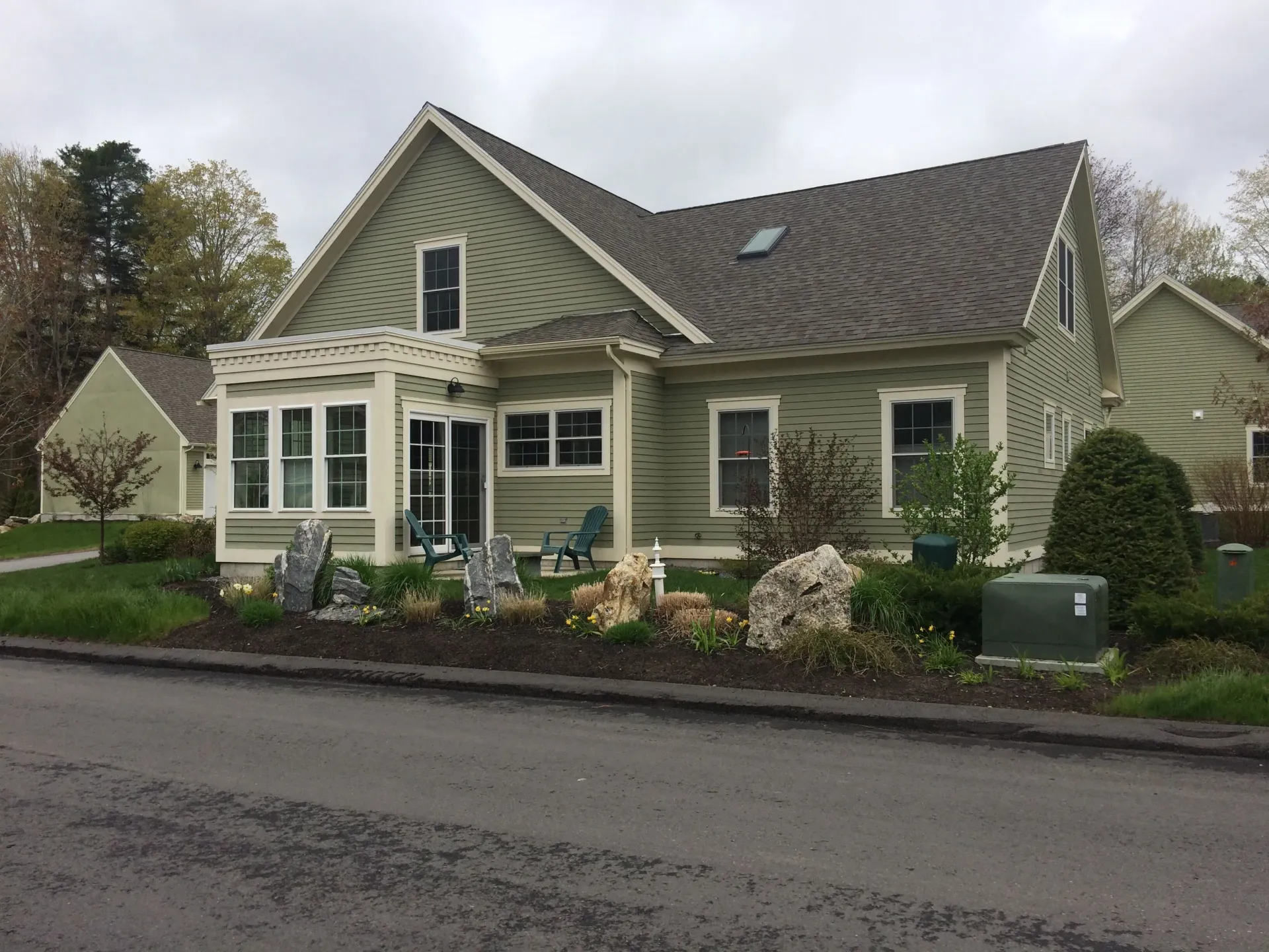 A green house with a gray roof is sitting on the side of the road.