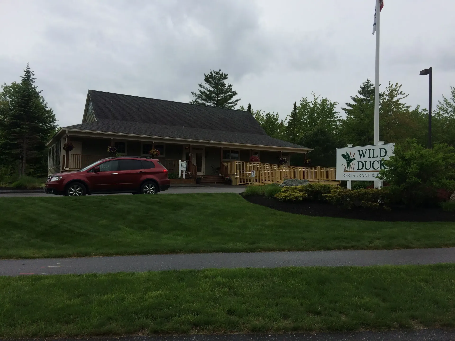 A red car is parked in front of a building that says wild duck