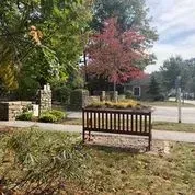 A wooden bench is sitting in the middle of a park next to a sidewalk.