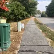 A sidewalk with a green trash can on the side of it next to a road.