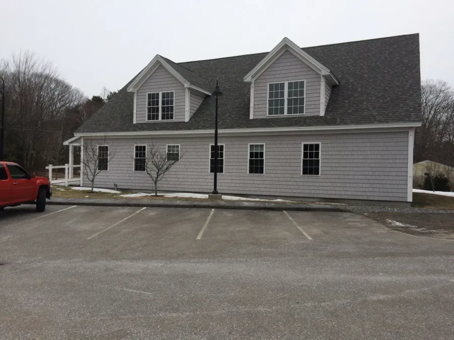 A red truck is parked in front of a large white house.