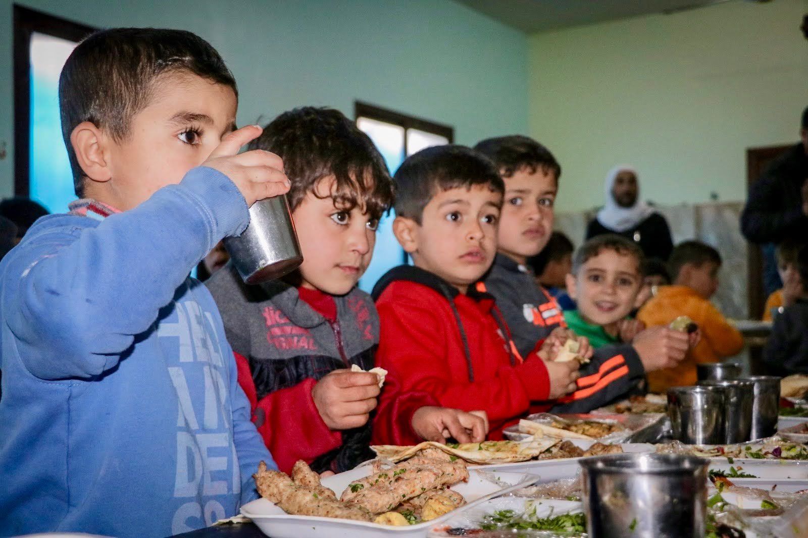 Un groupe d'enfants assis à une longue table, prenant un repas ensemble à l'intérieur.